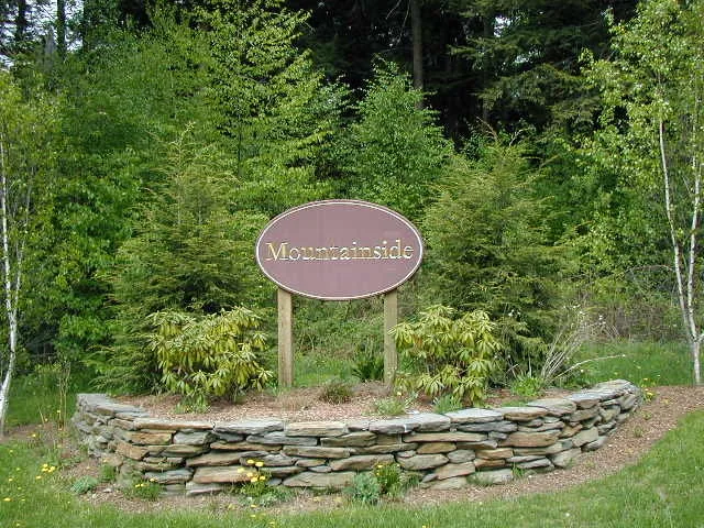 Oval Mountainside neighborhood sign on wooden posts above a curved fieldstone wall with landscaped shrubs