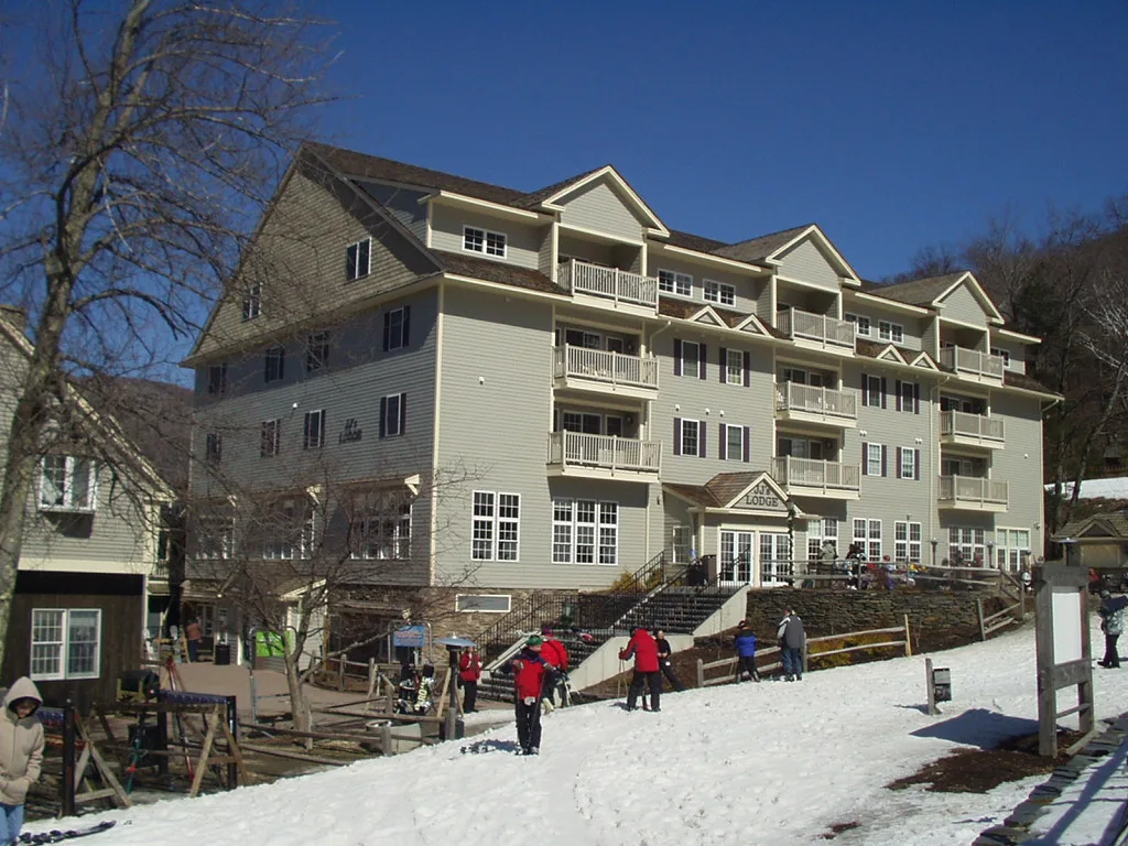 Four-story J.J.'s Lodge condominium building with balconies and skiers gathered on snow at the base