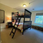Bunk bedroom with twin-over-full bunk bed, floral bedding, nightstand, mirror, and window seat with storage