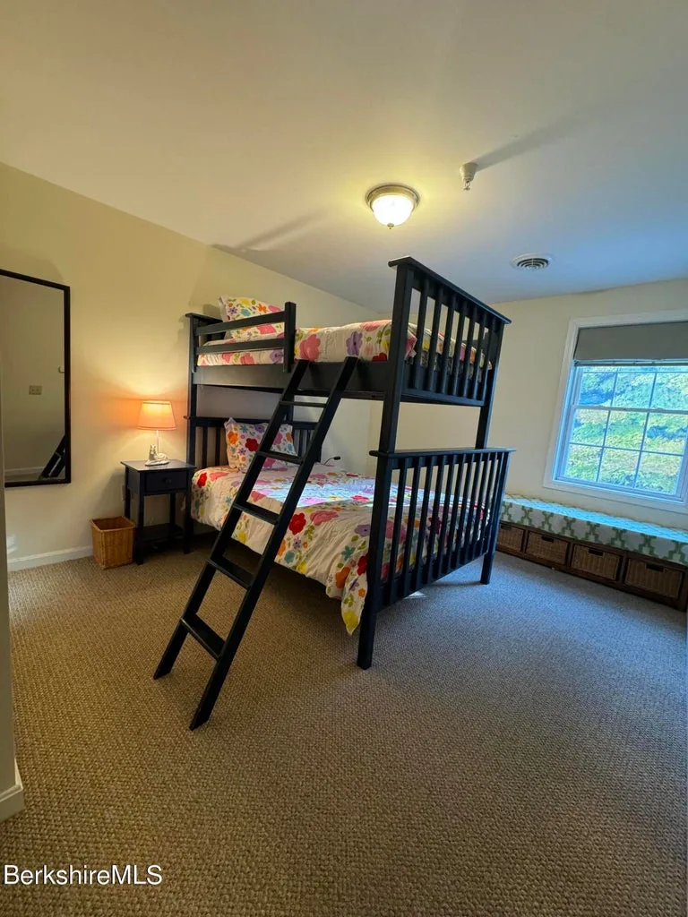 Bunk bedroom with twin-over-full bunk bed, floral bedding, nightstand, mirror, and window seat with storage