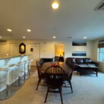 Dining table and bar stools at kitchen counter with leather sofa and mountain artwork in living room beyond