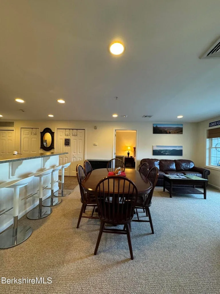Dining table and bar stools at kitchen counter with leather sofa and mountain artwork in living room beyond