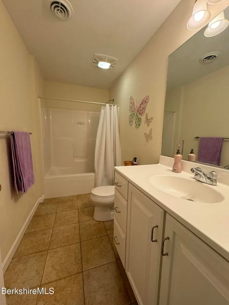 Guest bathroom with tub-shower combo, white vanity, toilet, and butterfly wall decor at JJ's Lodge 862