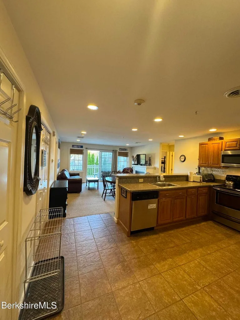 Open kitchen with tile floor, breakfast bar, and stainless dishwasher leading to carpeted living area