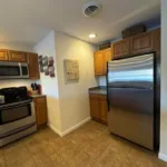 Kitchen corner with stainless refrigerator, electric range, oak cabinetry, and tile flooring