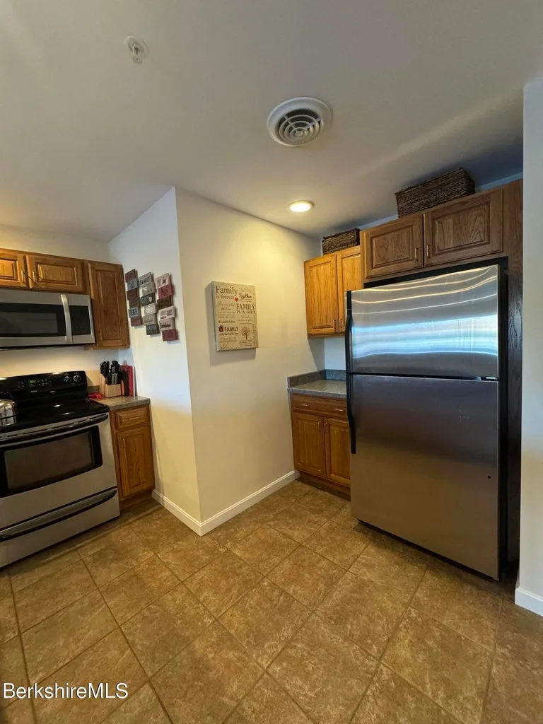 Kitchen corner with stainless refrigerator, electric range, oak cabinetry, and tile flooring