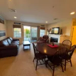 Carpeted living and dining area with leather sofa, dining table, fireplace, TV, and sliding door to balcony
