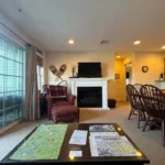 Living room with white-mantel gas fireplace, upholstered armchair, ottoman, and coffee table with trail maps