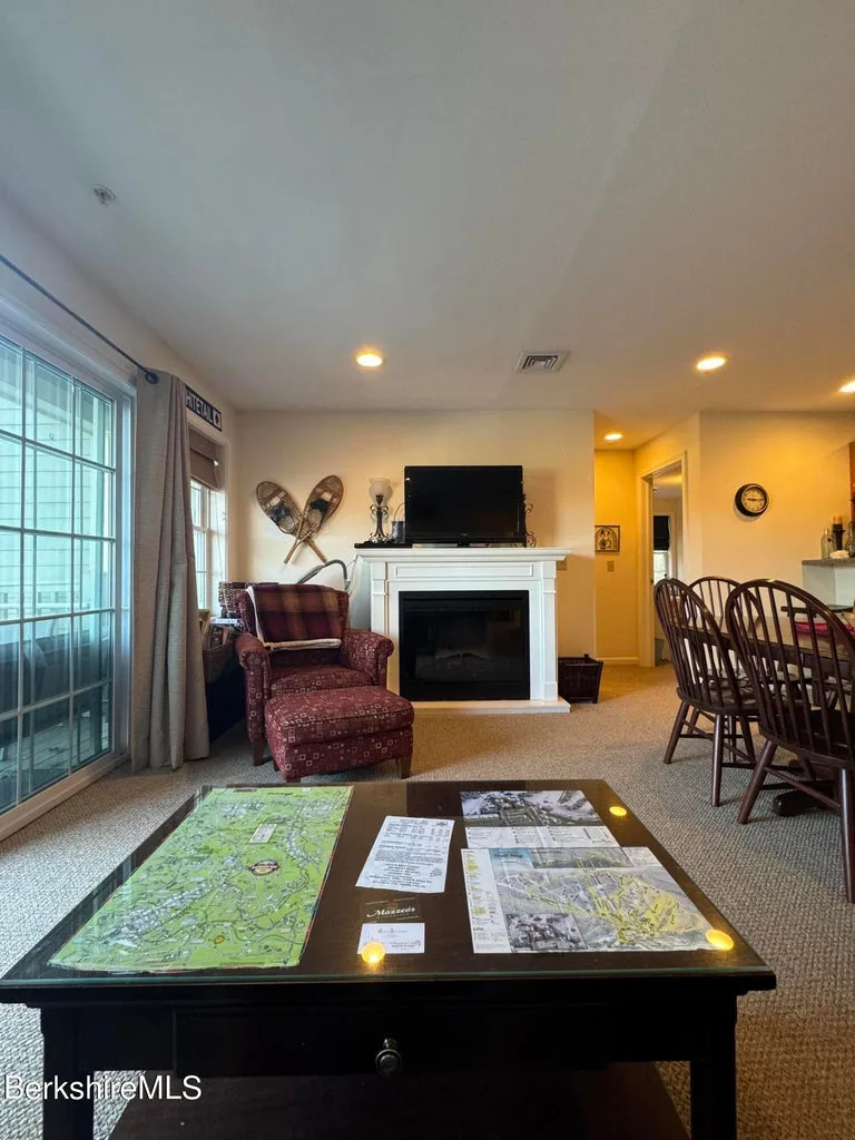 Living room with white-mantel gas fireplace, upholstered armchair, ottoman, and coffee table with trail maps