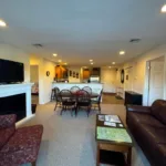 Open-plan view from living room across dining area to kitchen with leather sofa, fireplace, and entry door