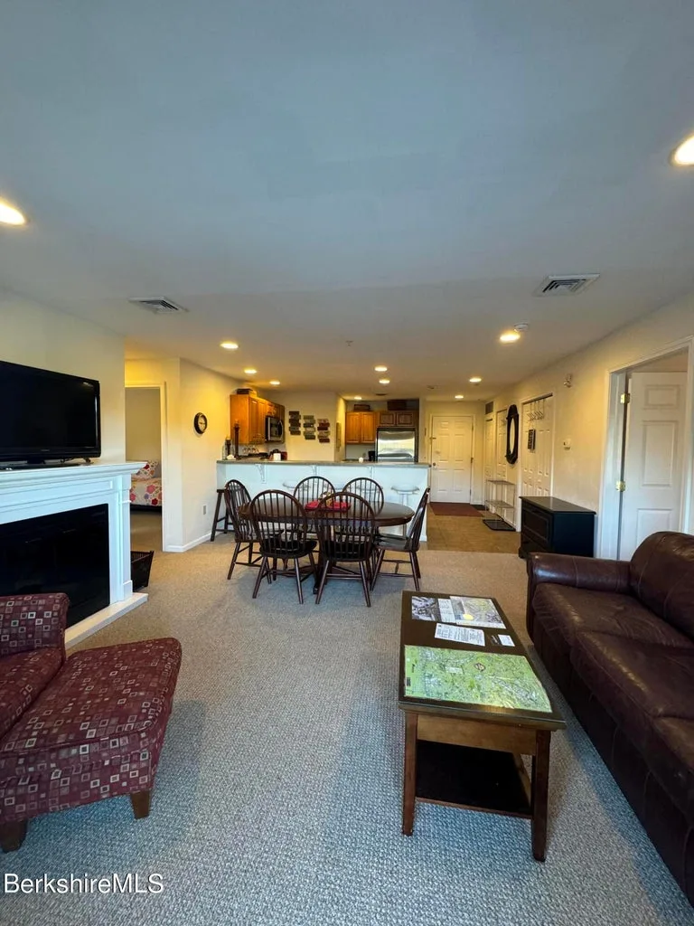 Open-plan view from living room across dining area to kitchen with leather sofa, fireplace, and entry door