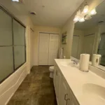 Primary bathroom with double-sink vanity, large mirror, glass-enclosed tub-shower, and tile flooring
