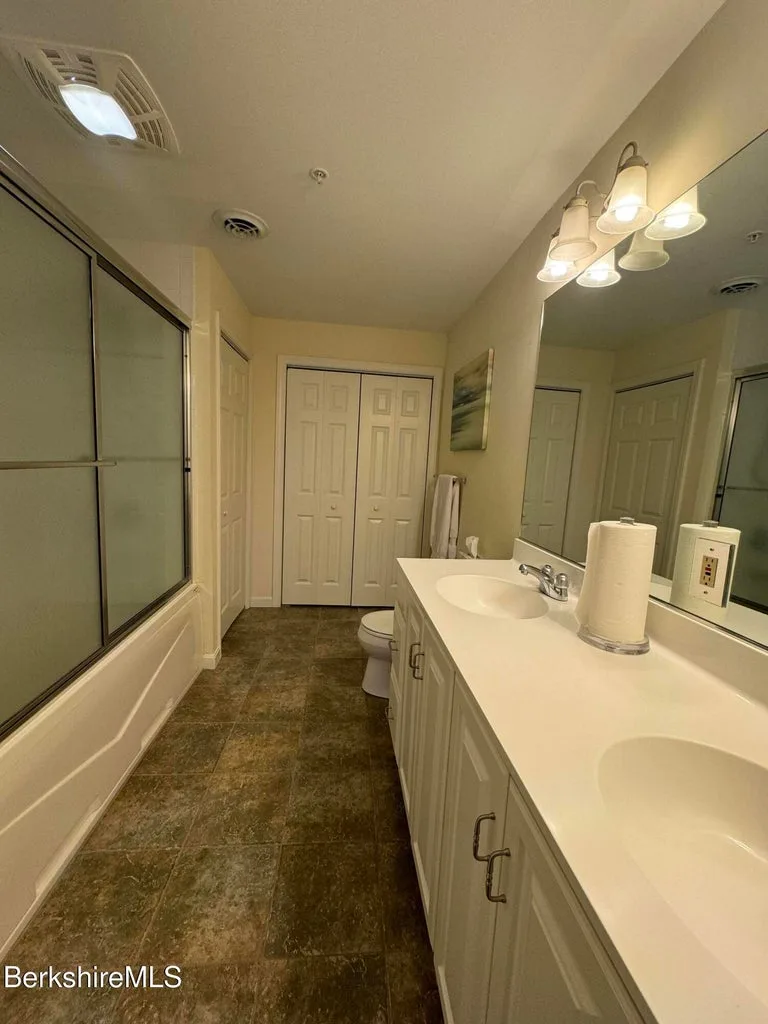 Primary bathroom with double-sink vanity, large mirror, glass-enclosed tub-shower, and tile flooring