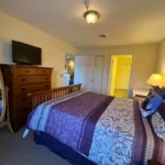 Primary bedroom with queen bed, wooden dresser, wall-mounted TV, and view to hallway and closet