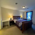 Second bedroom with queen bed, two nightstand lamps, white desk, and window with dark curtains