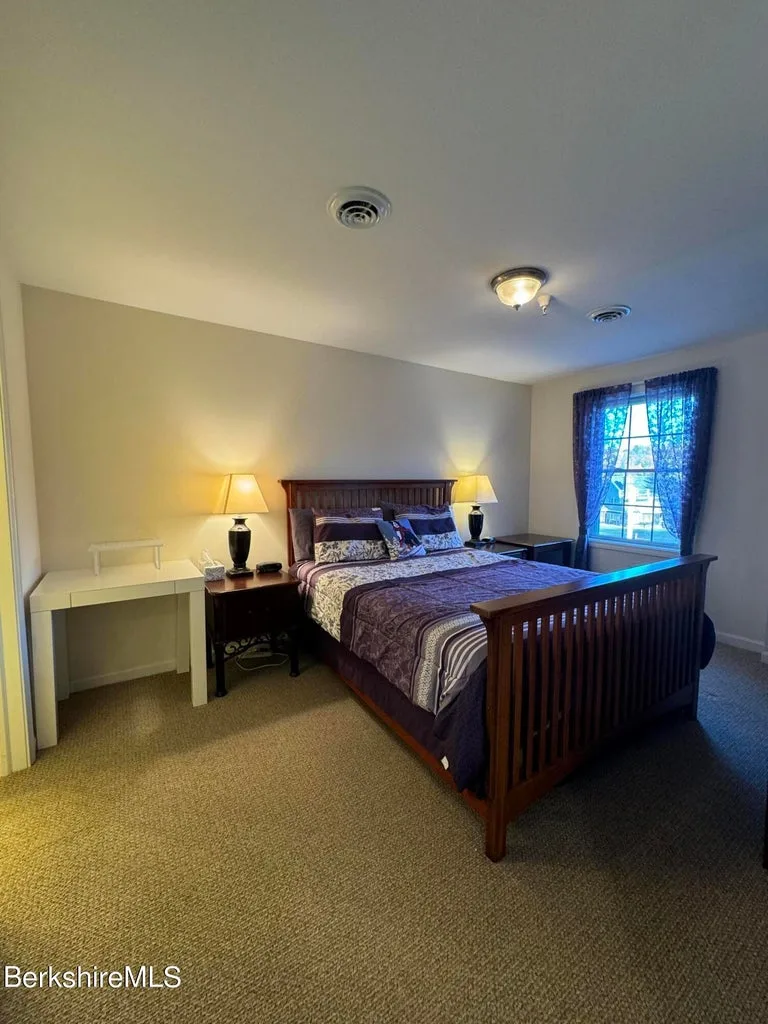 Second bedroom with queen bed, two nightstand lamps, white desk, and window with dark curtains