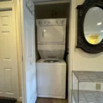 Stacked white washer and dryer in hallway closet beside ornate oval mirror at JJ's Lodge unit 862