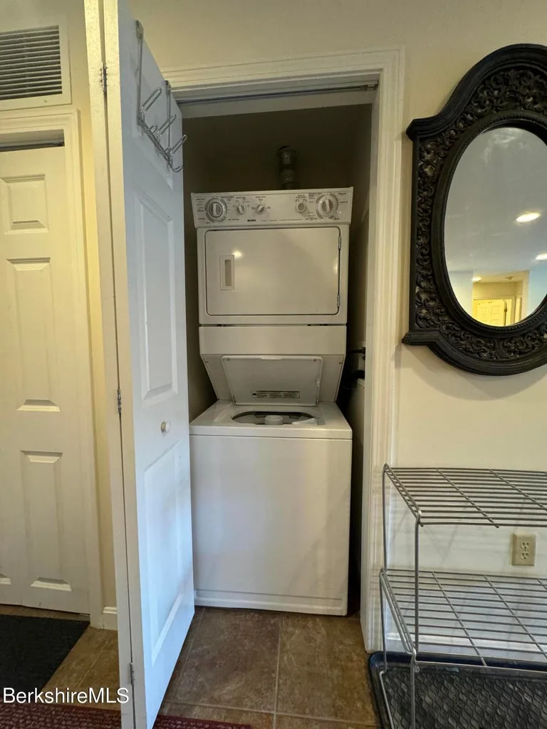 Stacked white washer and dryer in hallway closet beside ornate oval mirror at JJ's Lodge unit 862