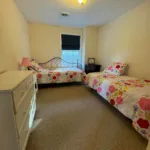 Bedroom with two twin beds, floral bedding, white dresser, and window with blackout shade