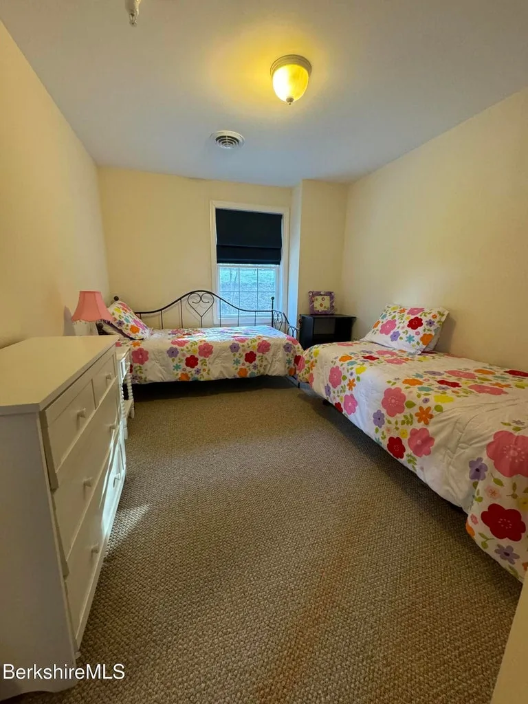 Bedroom with two twin beds, floral bedding, white dresser, and window with blackout shade